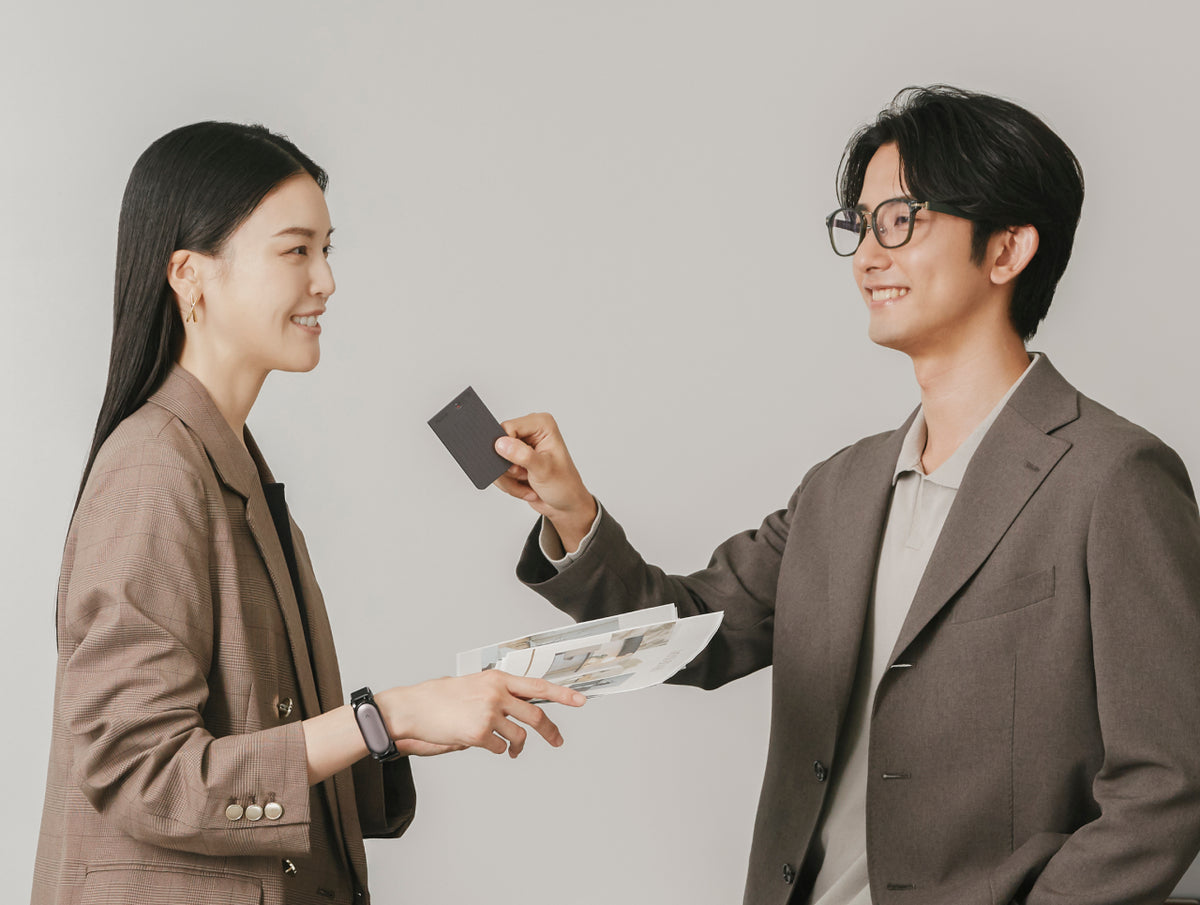 Plaud Noteを手にする男性とPlaud NotePinを着用した女性のビジネスシーン。