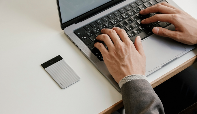 パソコンで作業中のデスクに置かれたシルバーのPlaud Note Pro。