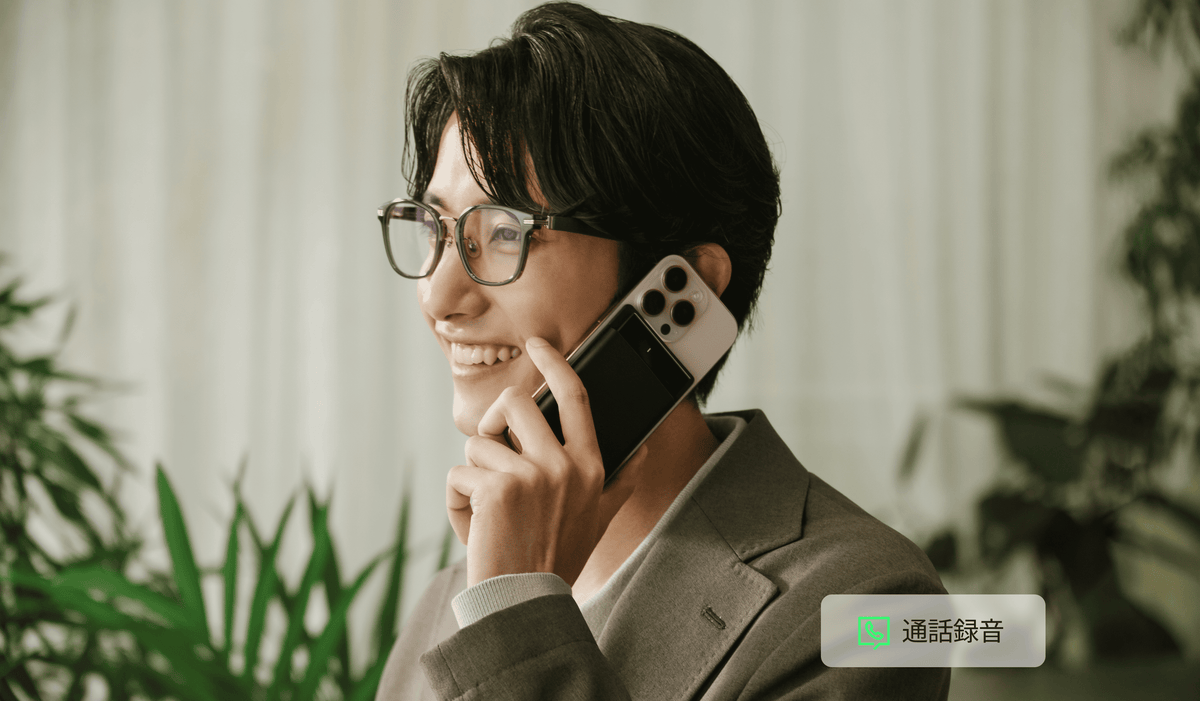 黒のPlaud Noteを装着したスマホで通話録音をしながら笑顔で話す男性。