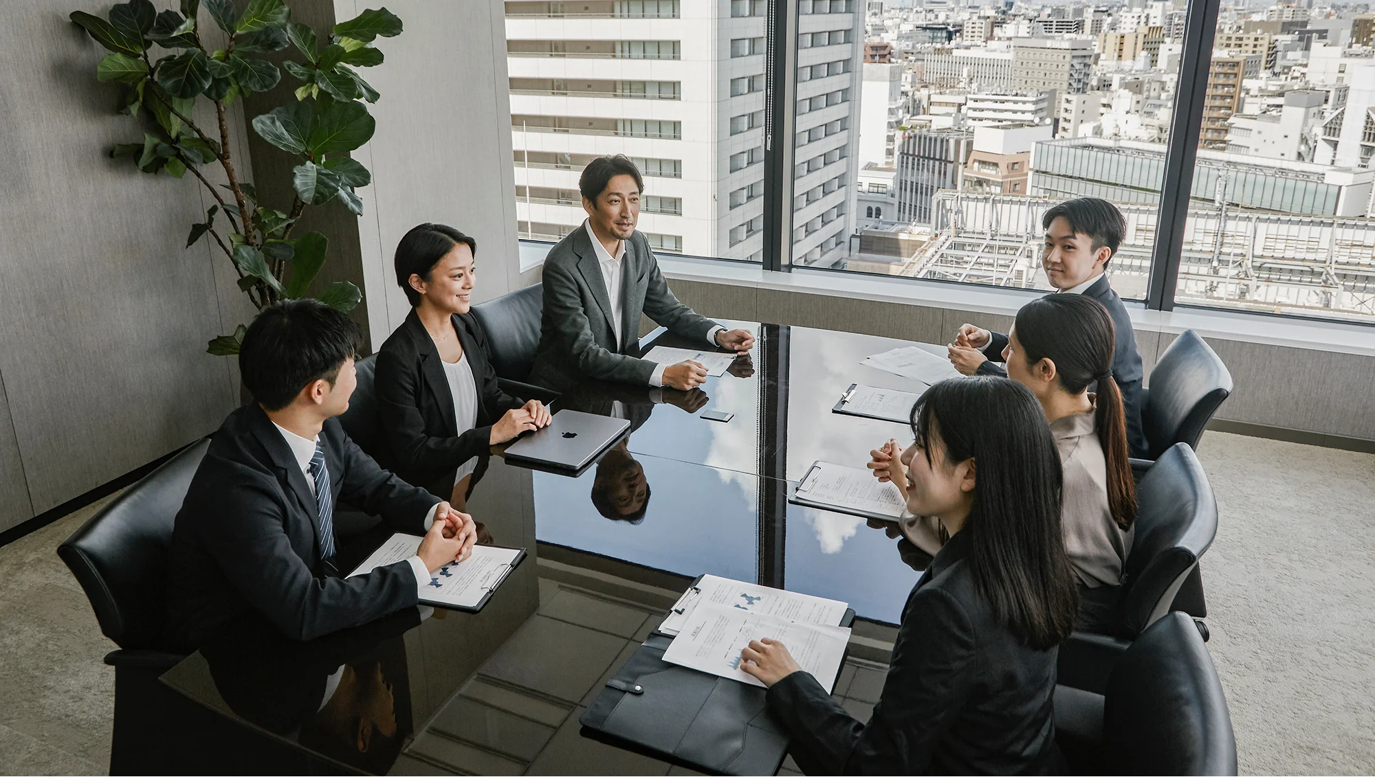 会議室のテーブルに置かれたシルバーのPlaud Noteと、打ち合わせを行うビジネスパーソン。